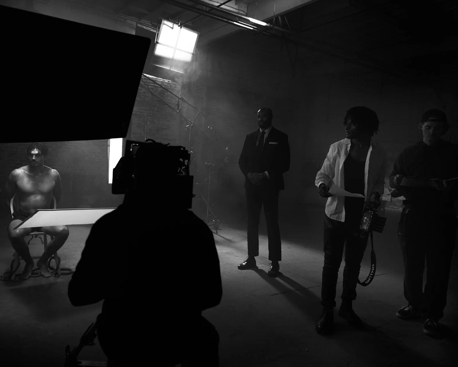 A crew silhouette facing the actors beneath film lights. The Hitman’s Dalliance.