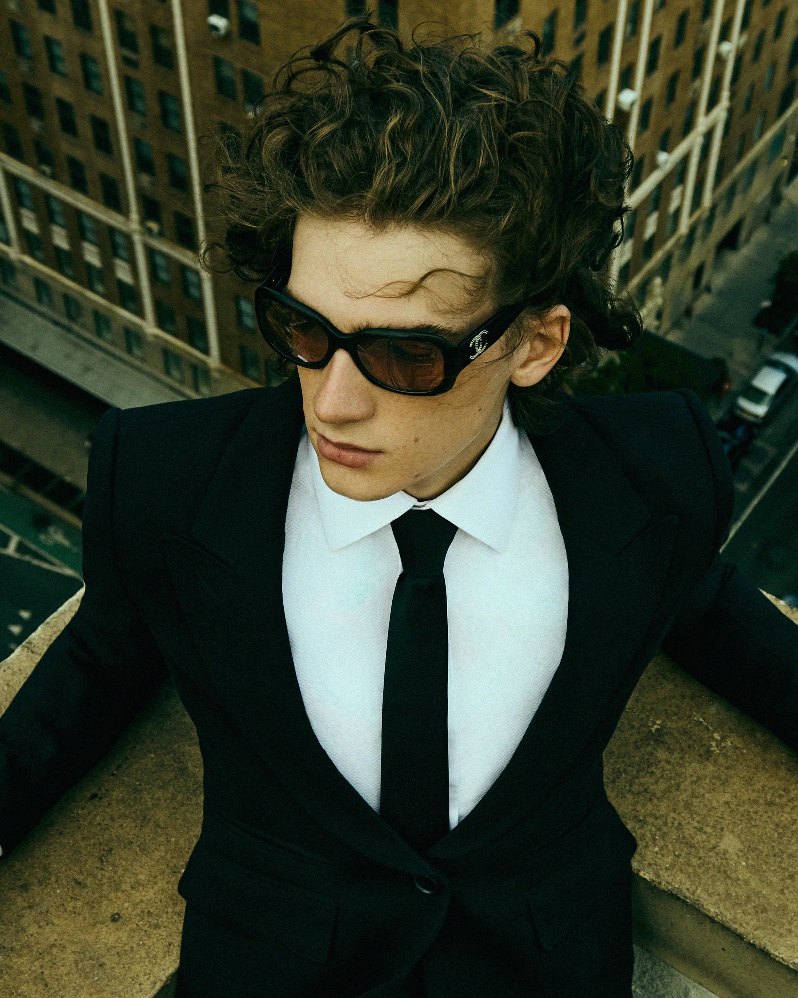 A model in black tailoring and sunglasses seen from above on a rooftop.