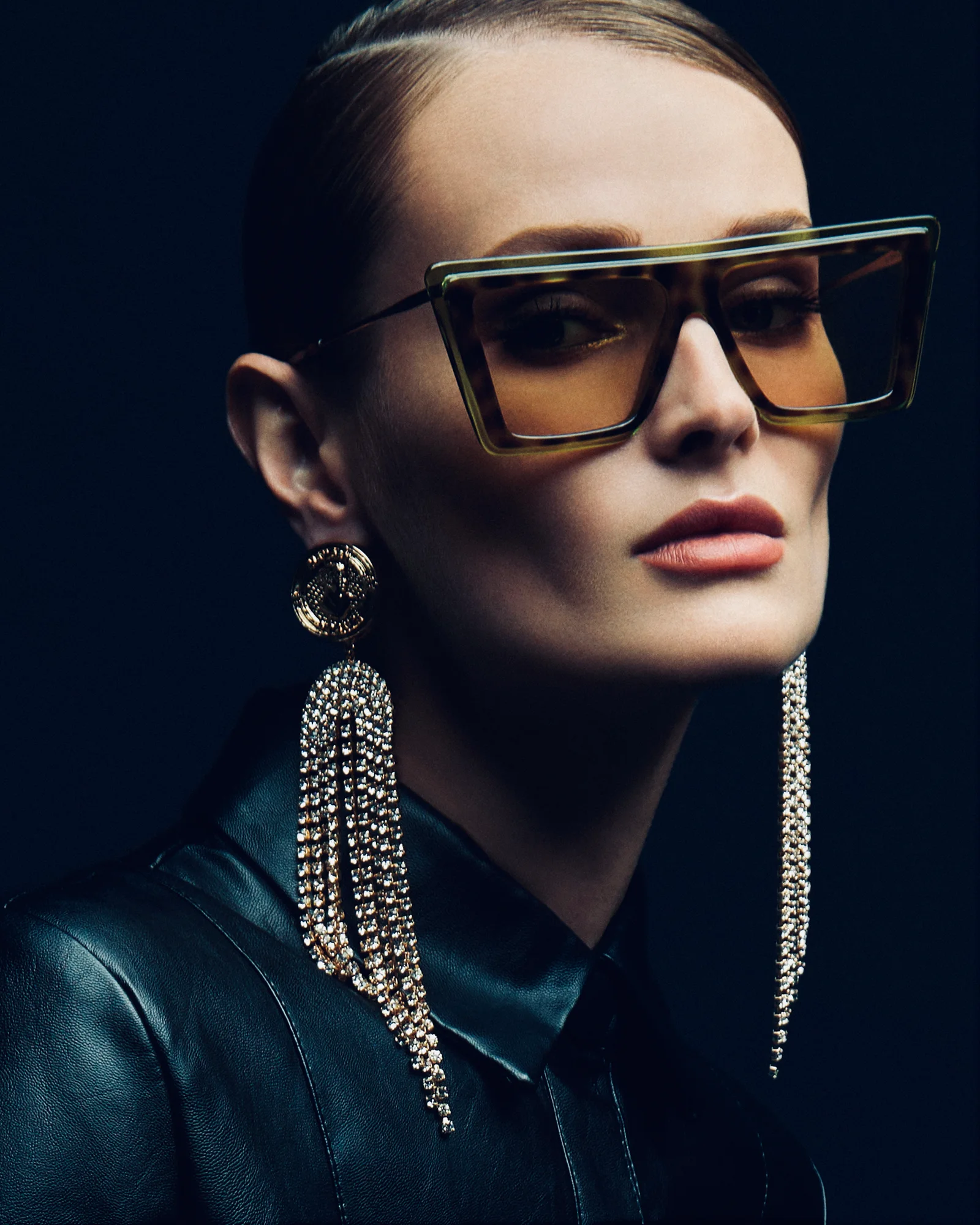 A close eyewear portrait with large framed sunglasses and long earrings.